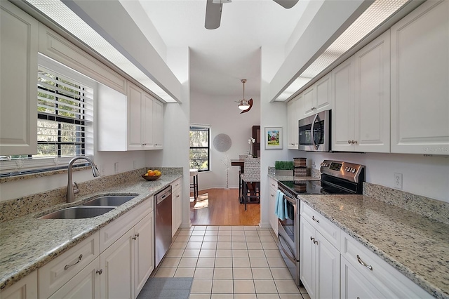 kitchen with sink, light tile patterned floors, appliances with stainless steel finishes, light stone counters, and white cabinets