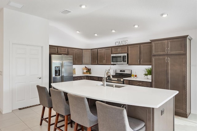 kitchen featuring tasteful backsplash, an island with sink, appliances with stainless steel finishes, and light tile patterned floors