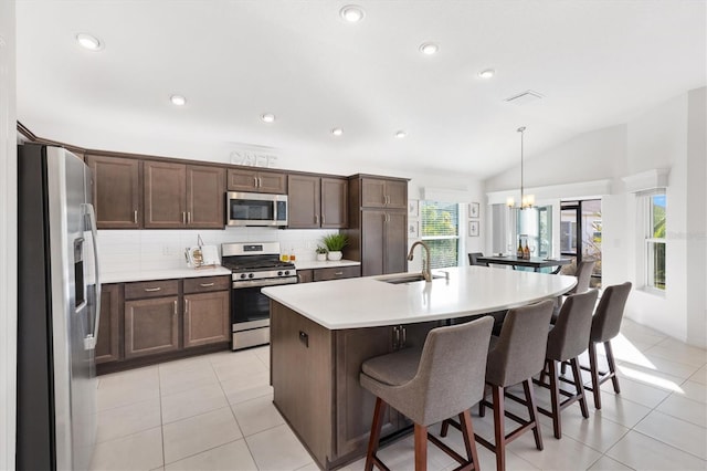 kitchen featuring lofted ceiling, sink, appliances with stainless steel finishes, a kitchen island with sink, and decorative light fixtures