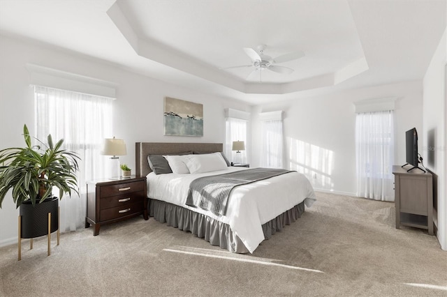 carpeted bedroom with a raised ceiling and ceiling fan