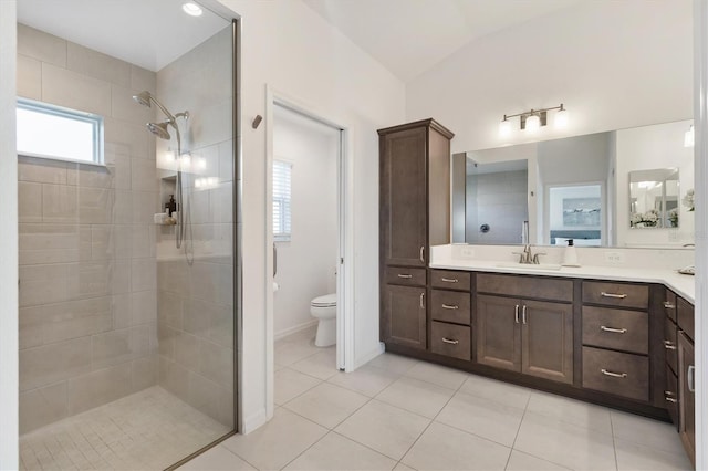 bathroom with toilet, vaulted ceiling, a tile shower, vanity, and tile patterned flooring