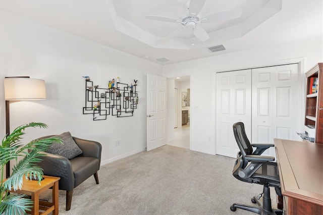 carpeted office space with ceiling fan and a tray ceiling