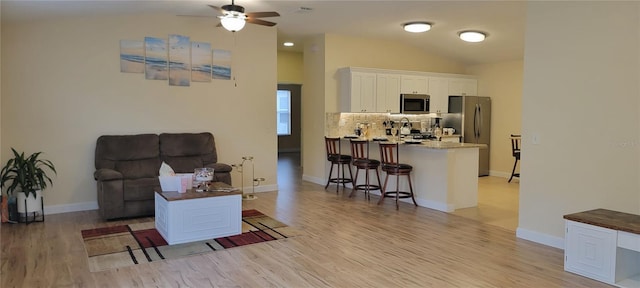 living room with lofted ceiling, ceiling fan, light wood finished floors, and baseboards