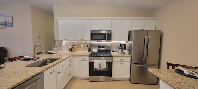 kitchen featuring stainless steel appliances, a sink, white cabinets, vaulted ceiling, and tasteful backsplash