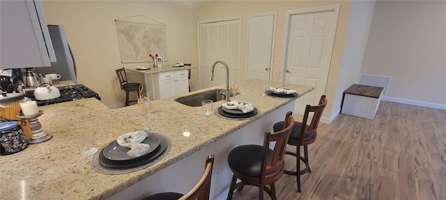 kitchen with a breakfast bar area, a peninsula, a sink, light wood-type flooring, and light stone countertops