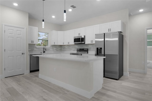 kitchen featuring a center island, appliances with stainless steel finishes, pendant lighting, light hardwood / wood-style floors, and white cabinets