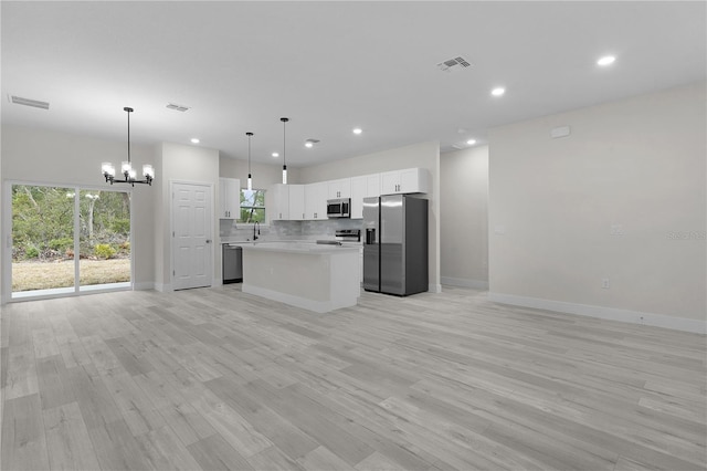 kitchen with appliances with stainless steel finishes, white cabinets, hanging light fixtures, a center island, and light wood-type flooring