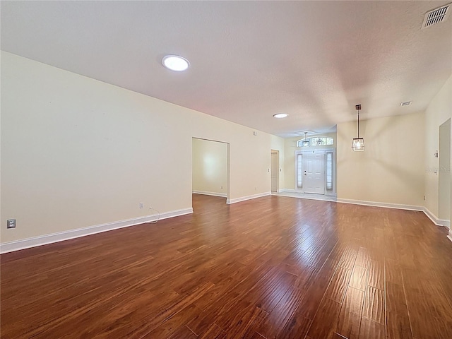 unfurnished living room with dark wood-style floors, visible vents, a textured ceiling, and baseboards