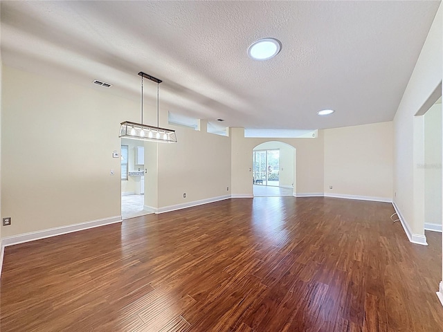 unfurnished living room with dark wood-style floors, arched walkways, visible vents, a textured ceiling, and baseboards