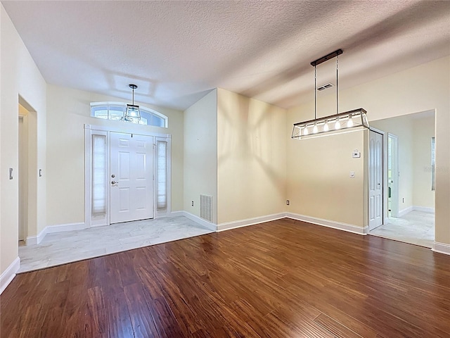 foyer entrance with visible vents, a textured ceiling, baseboards, and wood finished floors