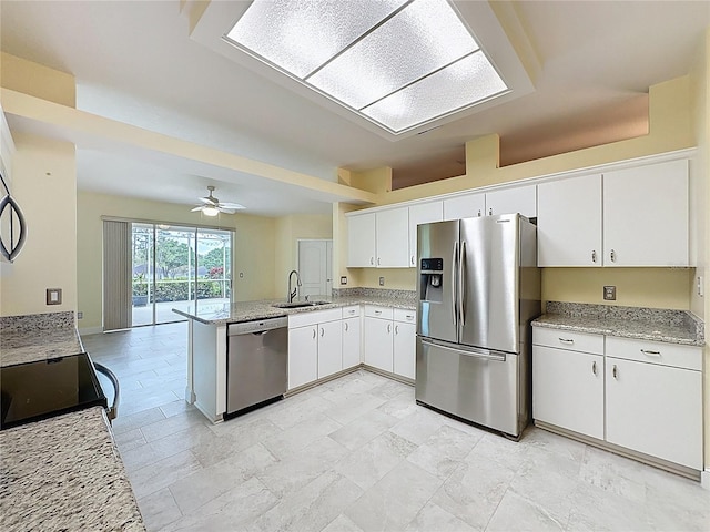 kitchen with light stone counters, stainless steel appliances, a peninsula, a sink, and white cabinets