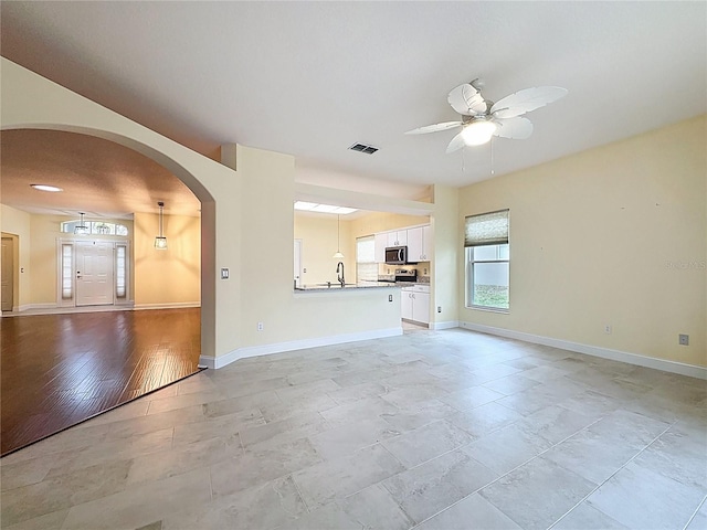 unfurnished living room with arched walkways, a sink, visible vents, baseboards, and a ceiling fan