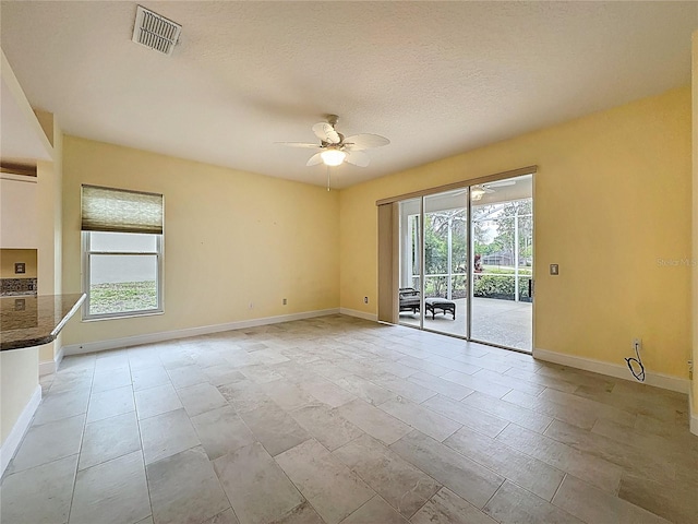 empty room with ceiling fan, a wealth of natural light, visible vents, and baseboards