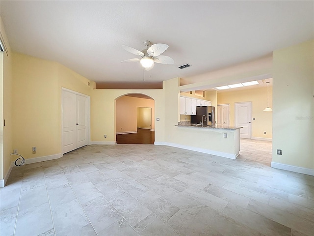 unfurnished living room with arched walkways, visible vents, a sink, ceiling fan, and baseboards