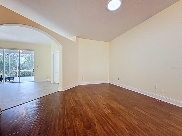 empty room with baseboards, arched walkways, and wood finished floors