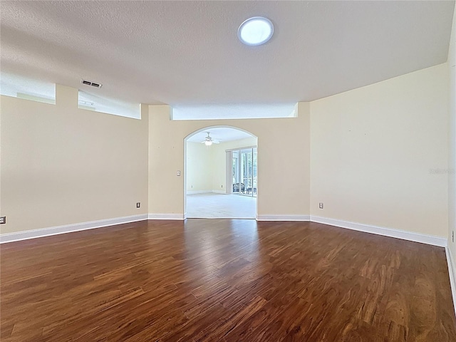 empty room with arched walkways, a textured ceiling, dark wood-style flooring, visible vents, and baseboards