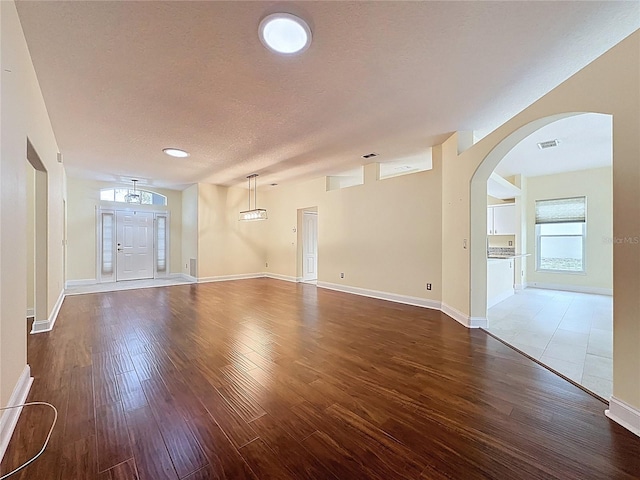 empty room featuring arched walkways, visible vents, a textured ceiling, wood finished floors, and baseboards