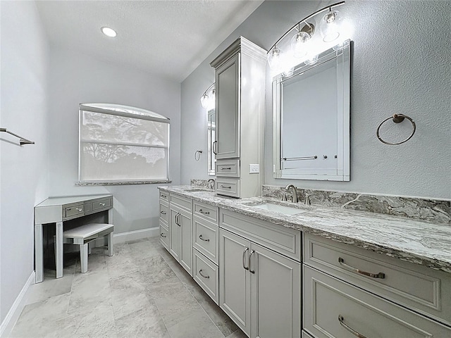 full bath featuring double vanity, marble finish floor, baseboards, and a sink