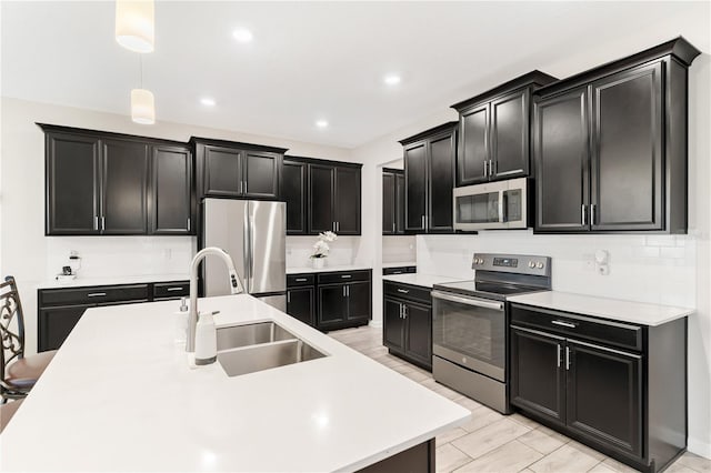 kitchen with sink, hanging light fixtures, a kitchen island with sink, stainless steel appliances, and light hardwood / wood-style floors