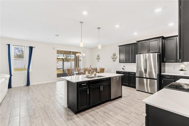 kitchen with pendant lighting, sink, an inviting chandelier, stainless steel appliances, and a center island with sink