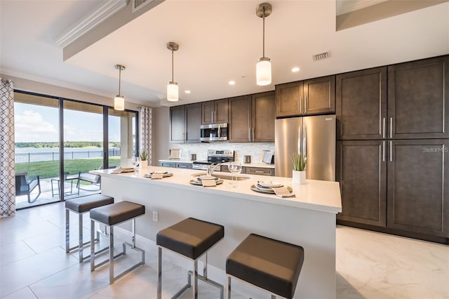 kitchen with decorative light fixtures, stainless steel appliances, an island with sink, and a kitchen breakfast bar