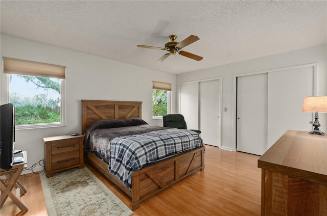 bedroom with ceiling fan, light wood-type flooring, multiple windows, and two closets