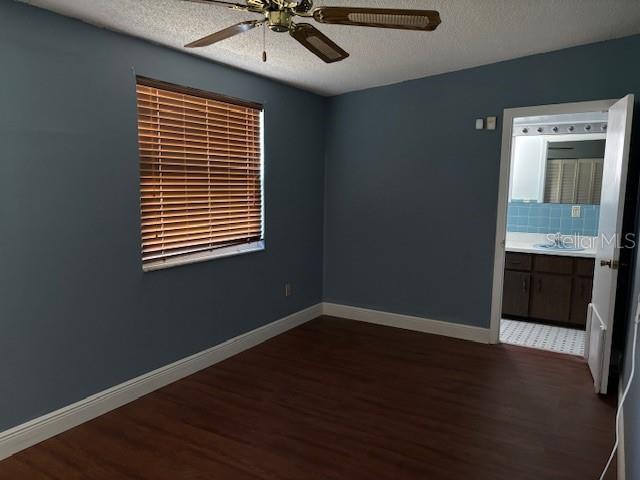 empty room featuring ceiling fan, dark wood-type flooring, sink, and a textured ceiling