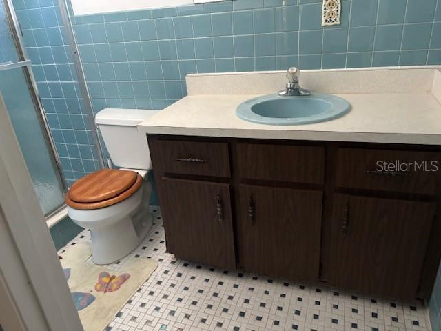 bathroom featuring tile patterned flooring, tile walls, vanity, a shower with shower door, and toilet