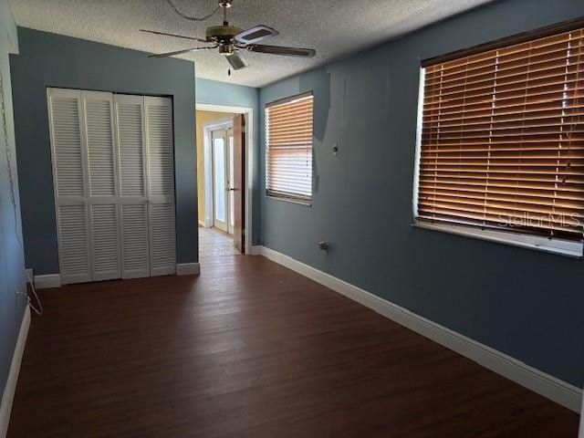 unfurnished bedroom featuring dark hardwood / wood-style floors, a textured ceiling, ceiling fan, and a closet