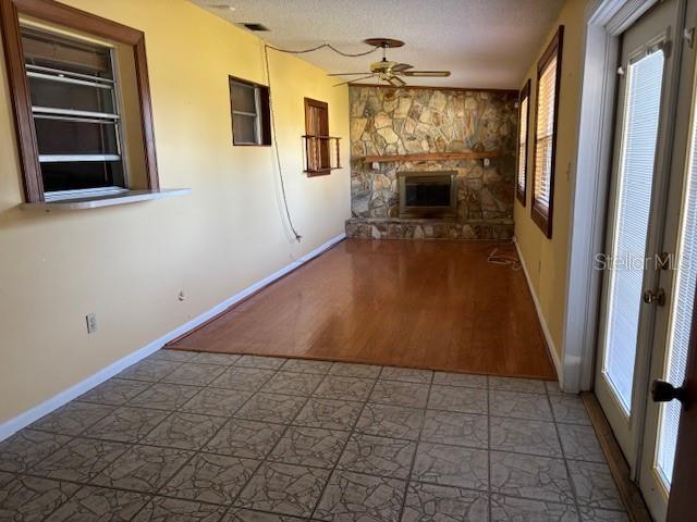 unfurnished living room with ceiling fan, a stone fireplace, french doors, and a textured ceiling