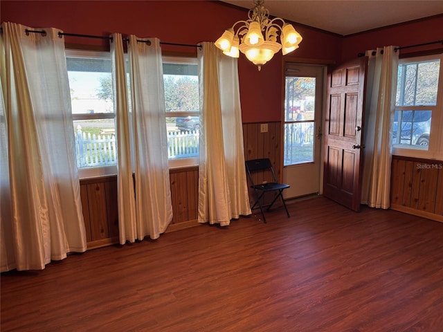 unfurnished dining area with ornamental molding, a chandelier, dark hardwood / wood-style flooring, and wood walls