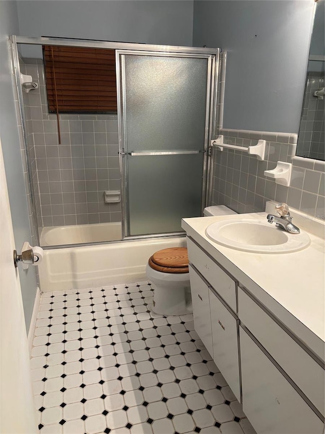 full bathroom featuring shower / bath combination with glass door, tile walls, tile patterned flooring, vanity, and toilet