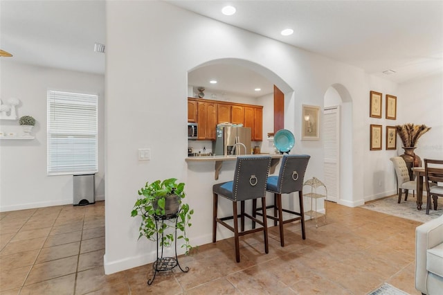 kitchen with appliances with stainless steel finishes, a breakfast bar area, light tile patterned floors, and kitchen peninsula