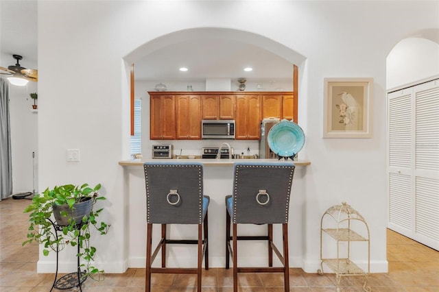 kitchen featuring light tile patterned flooring, range with electric cooktop, ceiling fan, and a kitchen bar