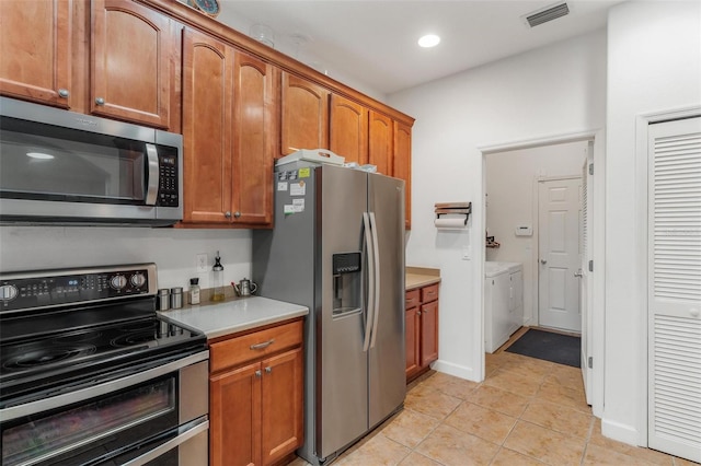 kitchen with light tile patterned floors, washer and dryer, and appliances with stainless steel finishes