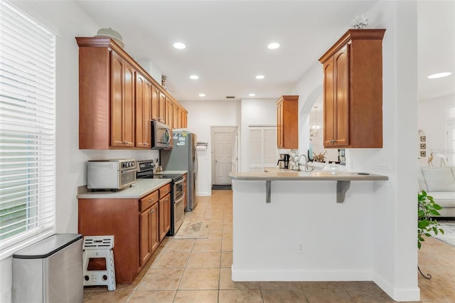 kitchen with a breakfast bar, sink, light tile patterned floors, kitchen peninsula, and stainless steel appliances