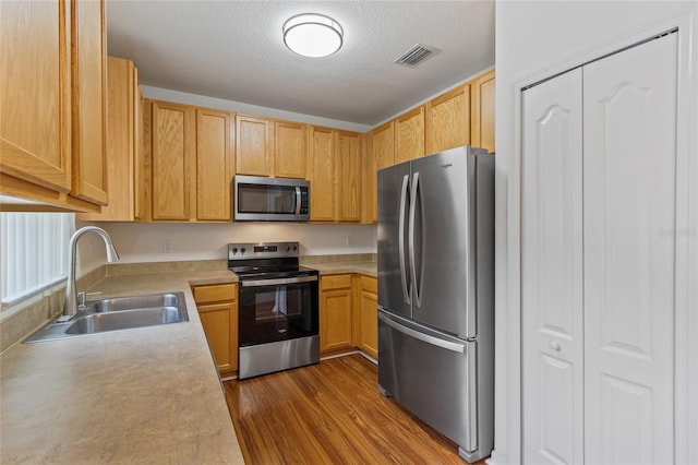 kitchen with sink, light brown cabinetry, stainless steel appliances, a textured ceiling, and dark hardwood / wood-style flooring