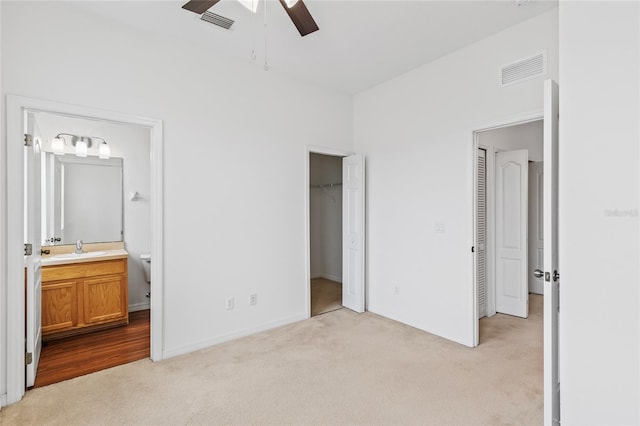 unfurnished bedroom with connected bathroom, sink, a walk in closet, light carpet, and ceiling fan