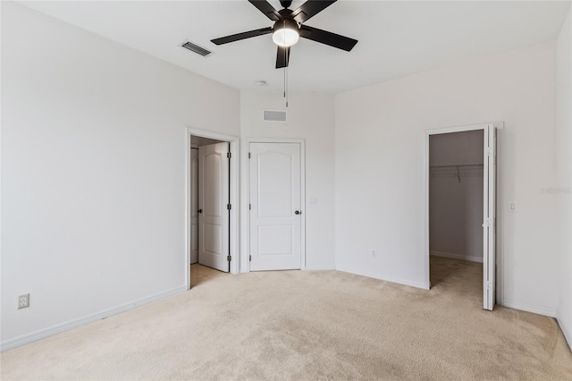 unfurnished bedroom featuring light carpet, a spacious closet, a closet, and ceiling fan