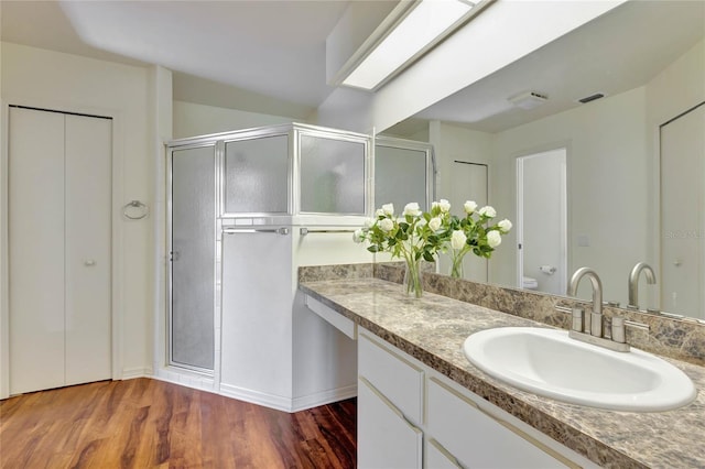 bathroom featuring hardwood / wood-style floors, a skylight, vanity, walk in shower, and toilet