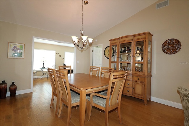 dining area with dark wood-type flooring, a chandelier, and vaulted ceiling