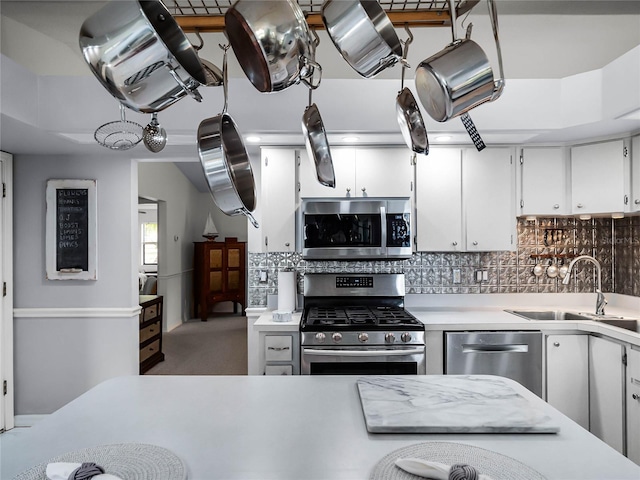 kitchen featuring appliances with stainless steel finishes, white cabinetry, carpet floors, sink, and backsplash