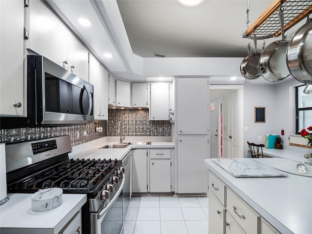 kitchen with sink, appliances with stainless steel finishes, white cabinetry, light tile patterned flooring, and decorative backsplash