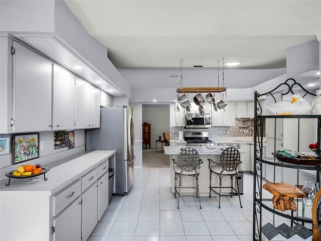 kitchen with a kitchen island, appliances with stainless steel finishes, white cabinetry, a breakfast bar area, and decorative backsplash