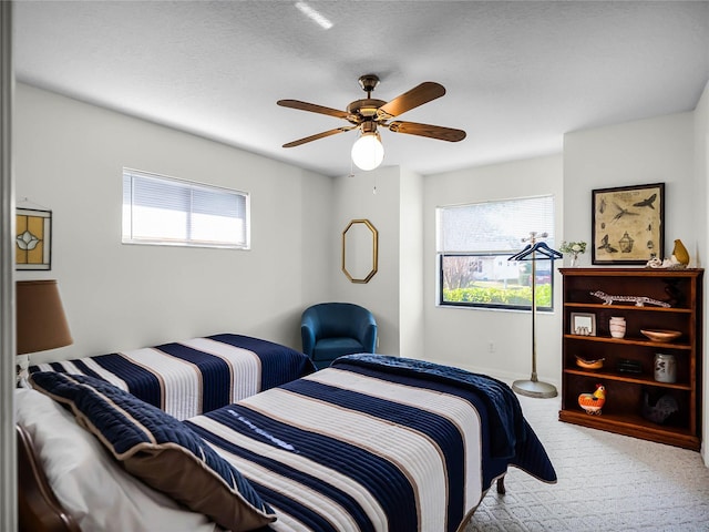 bedroom with ceiling fan, light colored carpet, multiple windows, and a textured ceiling