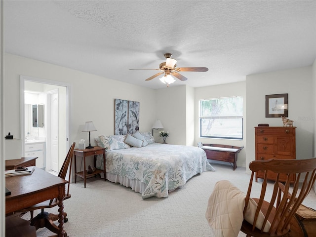 bedroom featuring ceiling fan, light colored carpet, connected bathroom, and a textured ceiling