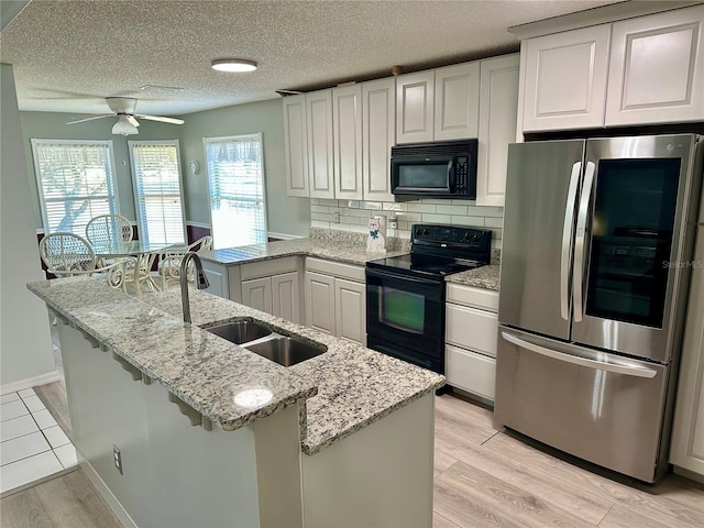 kitchen with sink, white cabinetry, tasteful backsplash, light stone countertops, and black appliances