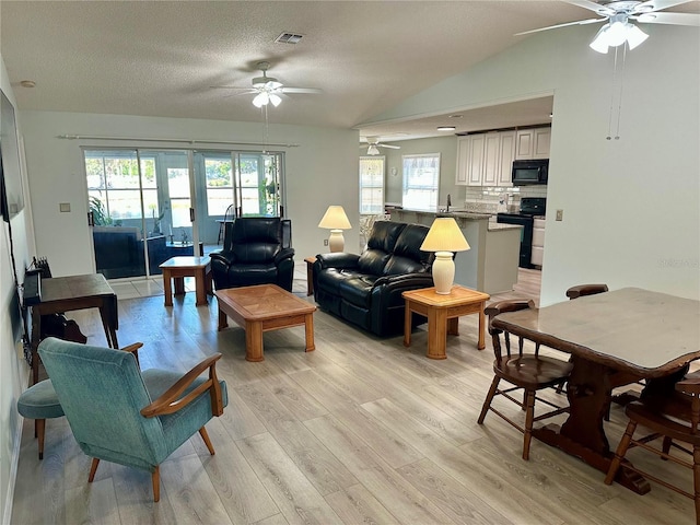 living room featuring sink, ceiling fan, light hardwood / wood-style floors, a textured ceiling, and vaulted ceiling