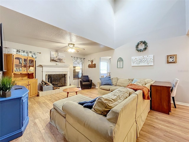 living room with a tile fireplace, ceiling fan, a high ceiling, light hardwood / wood-style floors, and a textured ceiling