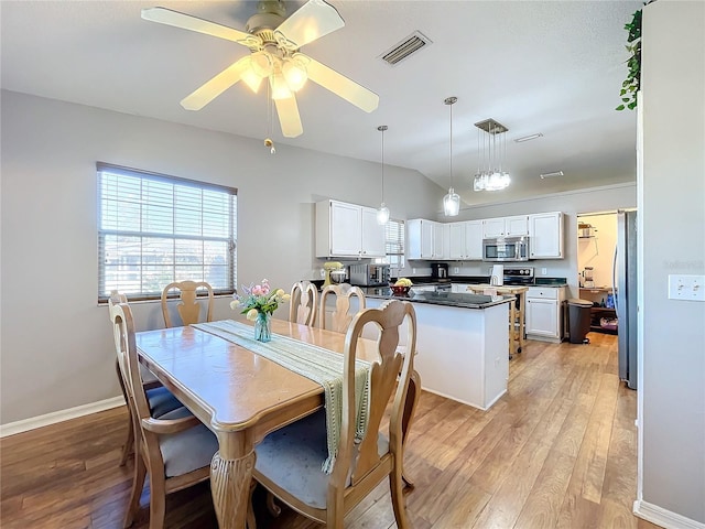 dining space featuring ceiling fan, vaulted ceiling, and light wood-type flooring